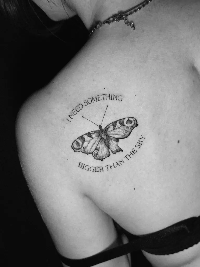 Farfalla tatuata sulla scapola con una breve scritta intorno.