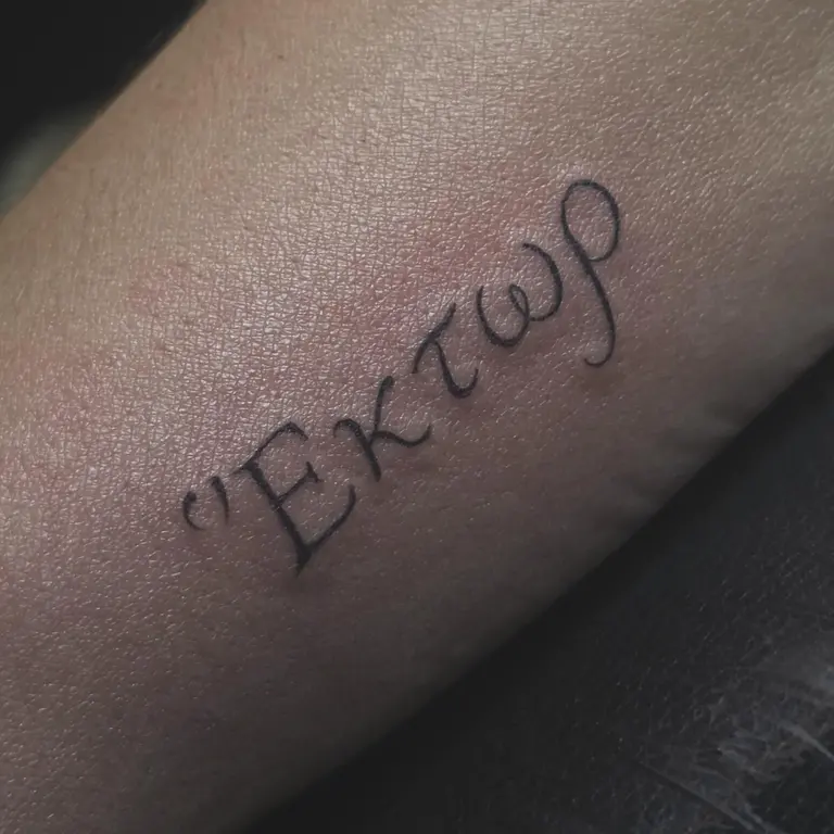 Piccolo lettering in caratteri greci tatuato su un arto.